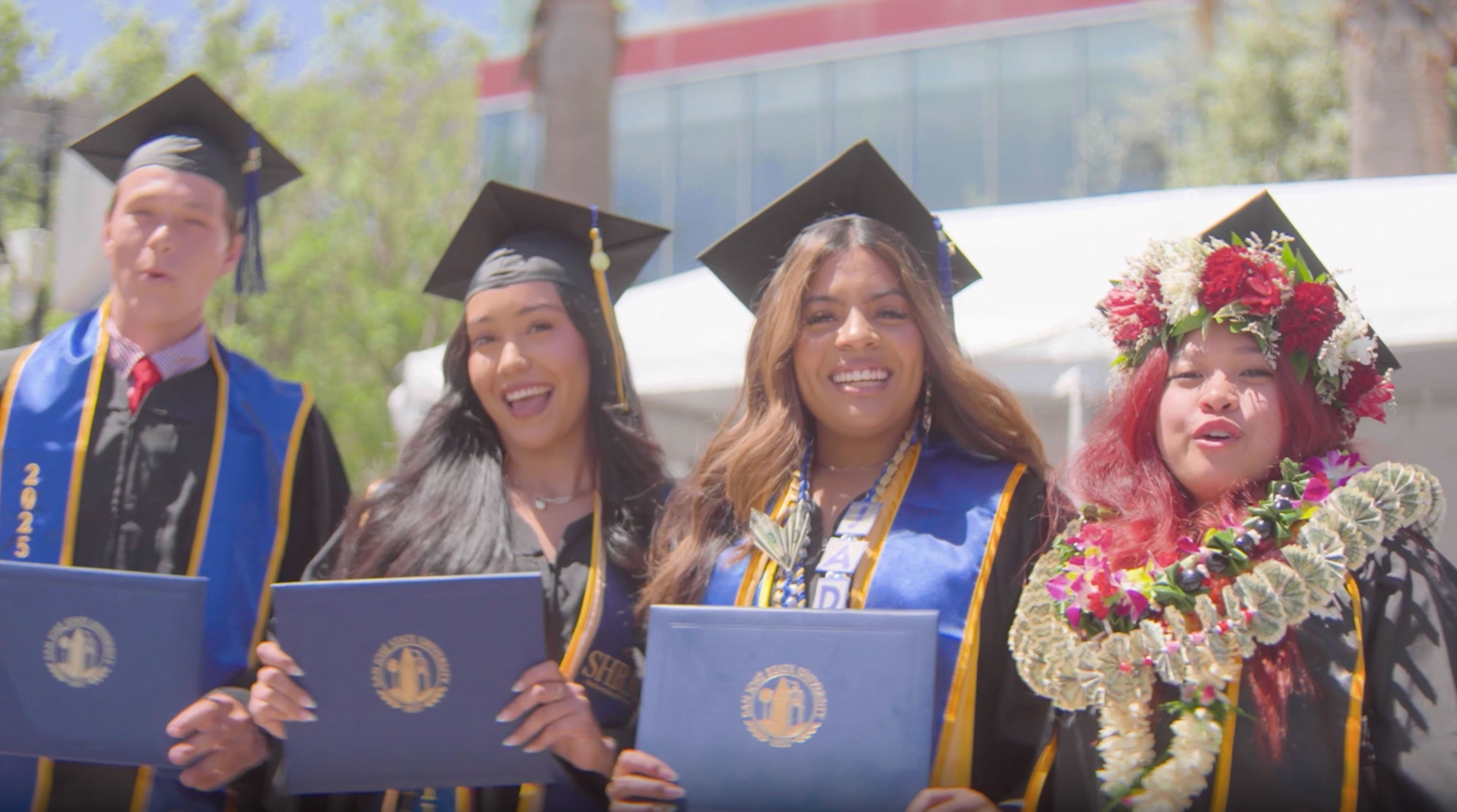Graduates posing for a group photo outside with their diplomas.